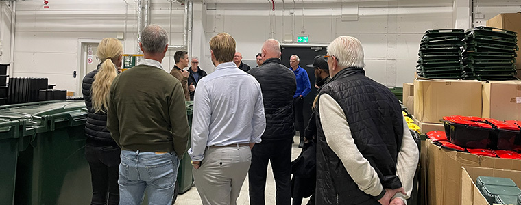 En grupp människor står mellan avfallspåsar och avfallskärl.