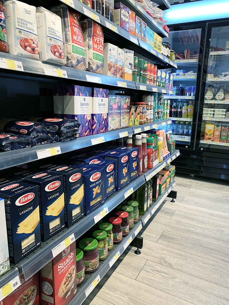 Bild på hyllor i matbutik med matvaror på. Bland annat syns pasta, ketchup, mjöl, socker, konserver mm.