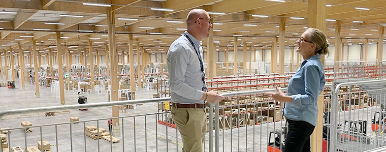 David Fröderberg från Elgiganten står på en balkong tillsammans med Caisa Björndal från Smuab. I bakgrunden syns Elgiganten stora lagerlokal.